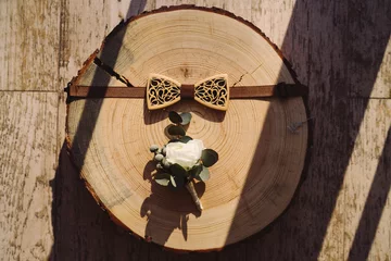Fotobehang groom's wooden bow tie and boutonniere on round piece of wood in sunlight © anna_gorbenko