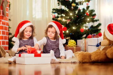 Fototapeta na wymiar Two little girls in caps of Santa Claus sitting on the floor wit