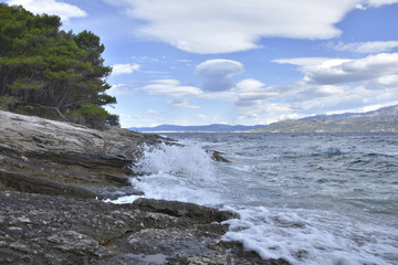 Waves against shore with mountain and blue sky in background, picture from Brac Island in Croatia.