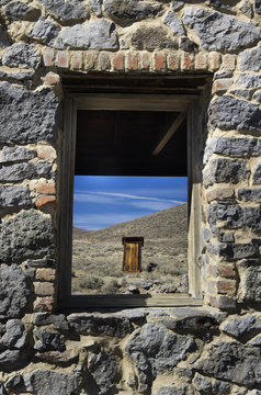 Gold mining ghost town outhouse in distance framed through stone building window;Bodie california united states of america