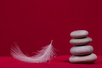 Gray stones and feather of bird on a red background. Items are in equilibrium closeup