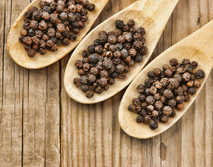 Black pepper in wooden spoon on the old board