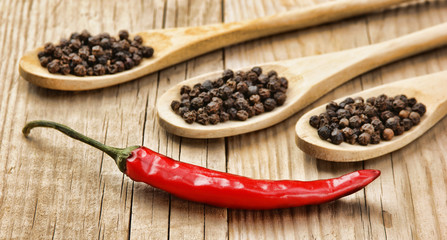 Black and red pepper in wooden spoon on the old board