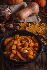 Autumn composition with pumpkin fried with garlic in a cast iron skillet on the old boards, with yellow maple leaves, walnuts and dried rose hips
