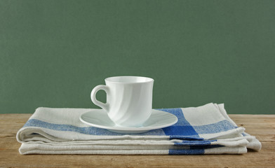 White coffee cup and dishcloth on old wooden table over green ba