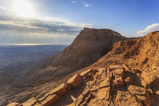 Rugged terrain and sunbeams at sunrise;Masada israel