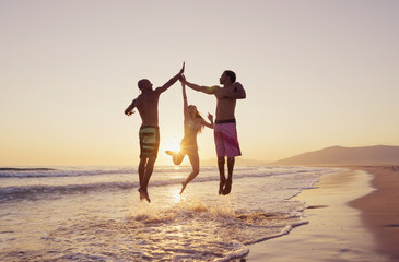 Three people leaping in the air to clap hands together on a beach at sunset;Tarifa cadiz andalusia spain