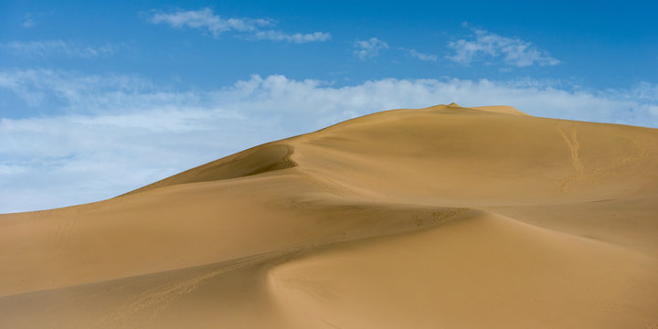 A large sand dune against a blue sky with cloud