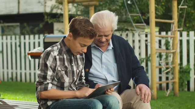 Young Boy Showing to  Senior Man how to use Touchscreen Tablet Computer