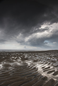 Rippled sand under a dark cloud at the water's edge;Northumberland england