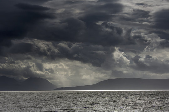 Dramatic sky with dark storm clouds over the ocean and a view of a silhouette of the coastline;Applecross peninsula scotland