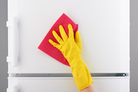 Hand in yellow glove cleaning refrigerator with pink rag