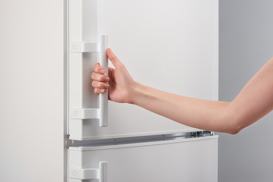 Female hand holding handle of white refrigerator door