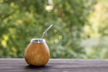 yerba mate in gourd matero on woooden table on green bokeh background. image with copy space