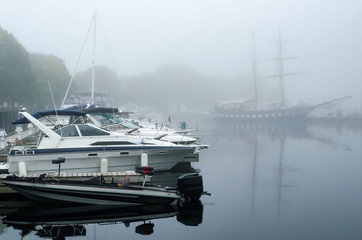 Fishing and powerboats moored on a foggy morning with a sailng ship in the background in contrast...
