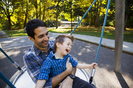 Father and son having fun together at playground on dish swing