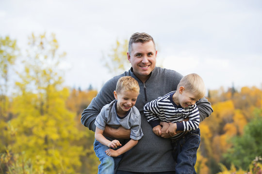 Father carrying two young sons in a park in autumn; Edmonton, Alberta, Canada