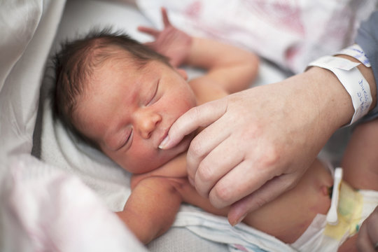 Newborn baby with eyes closed sucking on mother's pinky finger; Toronto, Ontario, Canada