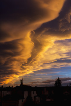 Dramatic colourful clouds at sunset with interesting formations and some blue sky with houses in a neighbourhood; Calgary, Alberta, Canada