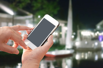 Hand holding mobile smart phone with blank screen in vertical position, blurred people background - mockup template