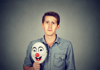 Young sad man with happy clown mask