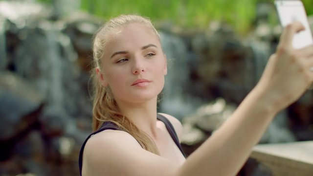 Sensual woman taking selfie in park. Close up of sexy girl taking photo with phone. Selfie woman. Blonde girl with sensual face expression taking selfie outside. Young woman smiling. Girl selfie