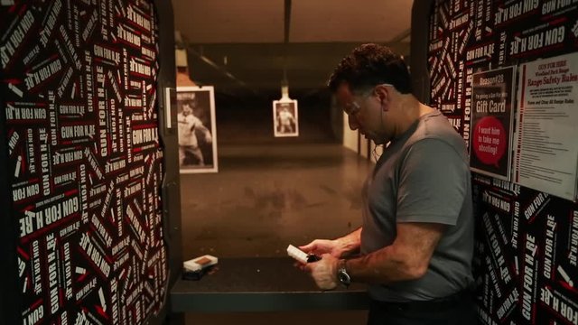 Indoor gun range, man reloads hand gun, with natural audio.