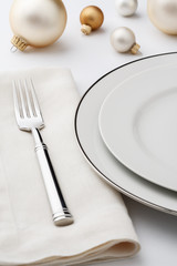 Festive fine dining Christmas table setting place setting with high quality classic style white china dishes, linen cloth napkin, silverware fork and decorations. Selective focus on tines of fork.