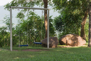 Two swings in the park with shade trees.
