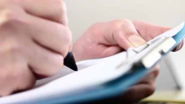バインダーの書類にペンで書く男性の手元クローズアップ：マクロレンズ使用ピント浅め