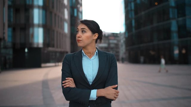 4k. Ultra HD. Portrait of young confident sexy caucasian businesswoman with arms crossed disapproval Your opinion. Pomade, brownhair, lady. Negation concept. Formal suit. Modern glass buildings bg