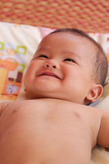 Asian baby smiling happily on bed.