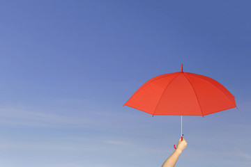 Red umbrella in hand on blue sky background.