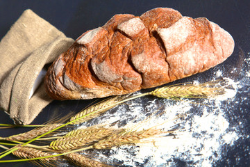 rustic crusty bread and wheat ears on a dark wooden table