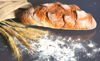 rustic crusty bread and wheat ears on a dark wooden table