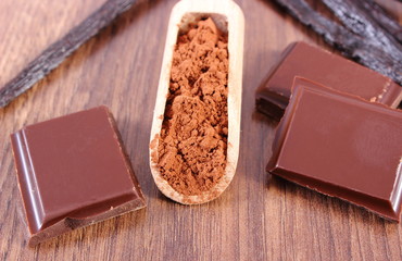 Powdery cocoa, dark chocolate, fragrant vanilla sticks on wooden surface