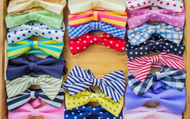 Collection of colorful bow ties with copy space in the middle on a wooden tray