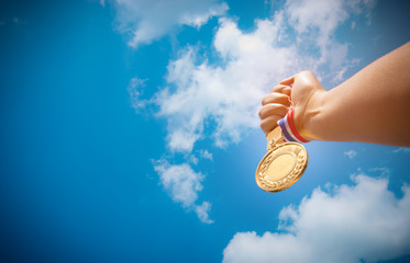 Fototapeta na wymiar hand raised and holding gold medal against blue sky. award conce