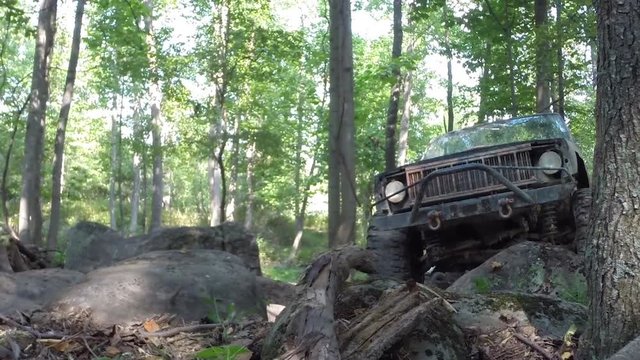 Jeep trails in woods, an off road truck slowly drives over big rocks.