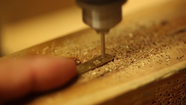 Person drills metal, a jeweler drills through a small piece of metal, closeup macro.