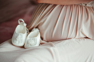 The pregnant girl looks at small shoes for baby
