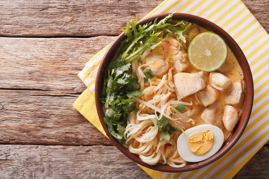 Malaysian laksa soup with chicken, egg, noodles and herbs close up in a bowl. horizontal top view