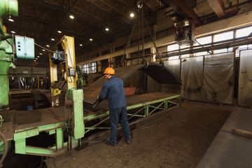 Fototapeta na wymiar worker in factory at metal skip machine putting work piece in. metalworking and bending