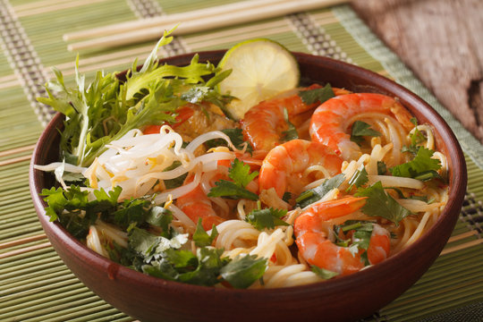 Malaysian laksa soup with shrimps, noodles and herbs close up in a bowl. horizontal