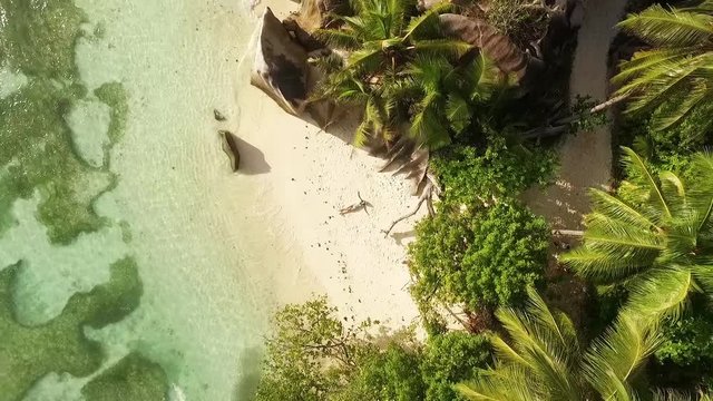 Aerial motion view of Seychelles tropical beach Anse Source D Argent at La Digue island with young woman sunbathing