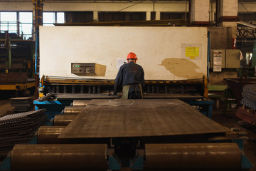 worker in factory at metal skip machine putting work piece in. metalworking and bending