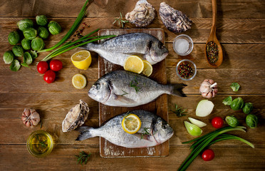 Fresh fish with herbs, spices and vegetables on  wooden backgrou