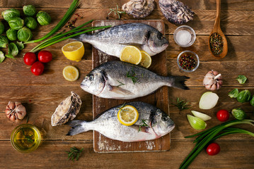 Fresh fish with herbs, spices and vegetables on a wooden backgro