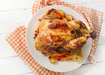 Whole roasted chicken with vegetables on a white plate.
