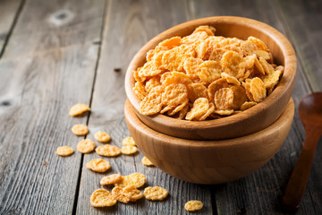 Cornflakes for breakfast in a bamboo plate on old wooden background. Selective focus.
